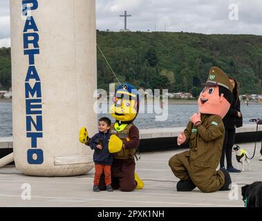 Un bambino che scatta foto con mascotte vestite in uniformi militari sulla strada con persone sullo sfondo Foto Stock