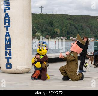 Un bambino che scatta foto con mascotte vestite in uniformi militari sulla strada con persone sullo sfondo Foto Stock