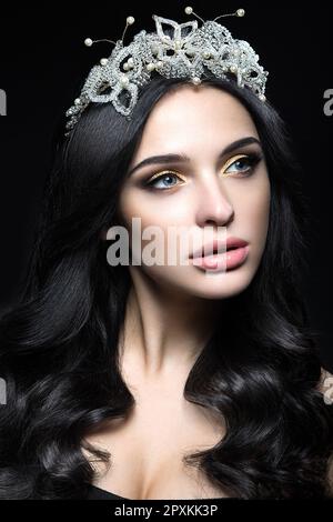 Bella donna dai capelli scuri con una corona di pietre preziose, ricci e trucco sera. Bellezza viso. Foto scattata in studio su sfondo nero. Foto Stock