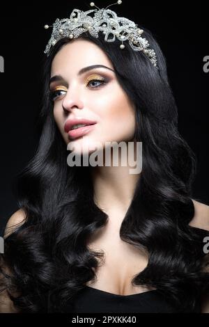 Bella donna dai capelli scuri con una corona di pietre preziose, ricci e trucco sera. Bellezza viso. Foto scattata in studio su sfondo nero. Foto Stock