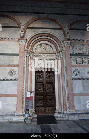 Una grande e imponente porta in legno con maniglia e cerniere in metallo, in piedi da soli in una parete di mattoni Foto Stock