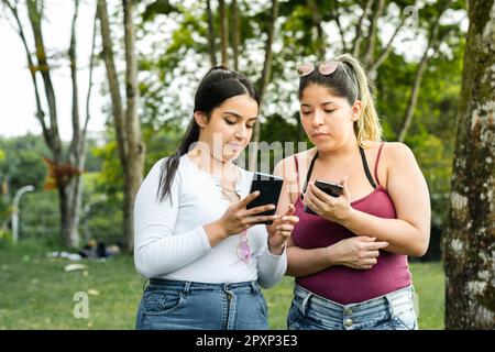 ragazza che mostra alla sua amica i messaggi di testo che ha sul suo telefono cellulare mentre fa una passeggiata nel parco. Foto Stock