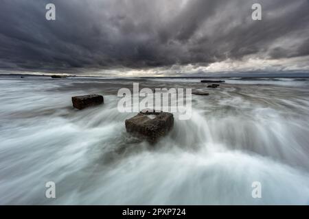 Una tranquilla scena oceanica caratterizzata da una serie di rocce aspre che si aggettano dall'acqua, con onde che si schiantano contro di loro Foto Stock