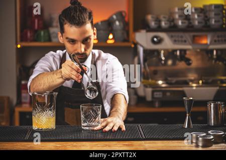 Barman che mette la sfera di ghiaccio nel vetro vecchio stile Foto Stock