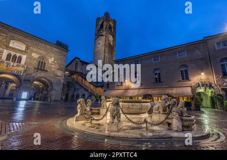 Torre Civica chiamata Campanone nel centro storico. Palazzo della ragione (a sinistra) e Palazzo del Podesta (a destra) con fontana in Piazza Vecchia al crepuscolo Foto Stock