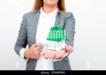 Donna d'affari in un vestito grigio che tiene una casa di carta colorata in una mano. Foto Stock
