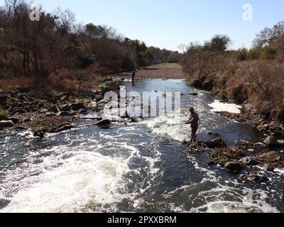 Immagine di 2 uomini che pescano in una parte infuriante del fiume del coccodrillo in Sudafrica , presa in inverno quando il terreno e le piante sono più asciutte e marroni Foto Stock