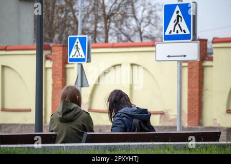 Due persone sedute su una panchina, una di loro ha un segno blu che dice pedonale. Foto Stock