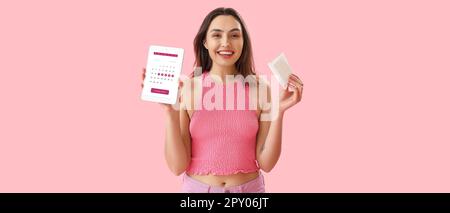 Felice giovane donna che tiene il pad mestruale e tablet computer con calendario aperto sullo schermo su sfondo rosa Foto Stock