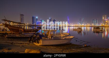 Barche a motore sulla riva del Golfo Persico con centro illuminato sullo sfondo, Manama, Bahrain Foto Stock