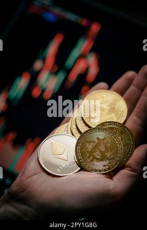 Mano che tiene varie monete di criptovaluta d'oro con grafico a bastone di candela e sfondo digitale. Bitcoin, Ethereum, Litecoin, Dogecoin. Foto Stock