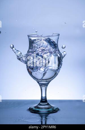 L'immagine di versare acqua potabile, in un vetro rotto, che fa sentire rinfrescato su sfondo bianco sfocato, spruzzi d'acqua, acqua frizzante, Foto Stock