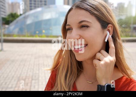 Primo piano di una ragazza ridente che collega le sue cuffie wireless con un dito nella metropoli moderna di San Paolo Foto Stock