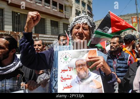 Un protettore tiene un ritratto del defunto prigioniero palestinese Khader Adnan durante uno sciopero generale. Protesta contro la morte di Khader Adnan nella prigione israeliana dopo uno sciopero della fame durato 87 giorni, il primo ministro palestinese Muhammad Shtayyeh ha affermato che l'occupazione ha compiuto un assassinio contro Adnan rifiutandosi di chiedere il suo rilascio e trascurandolo dal punto di vista medico, E il Ministero degli Affari Esteri palestinese ha ritenuto il governo israeliano pienamente responsabile del "crimine che ha portato alla morte di Khader Adnan”. Foto Stock