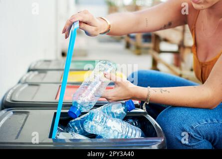 Ripulire i nostri oceani attraverso il riciclaggio. una donna irriconoscibile accovacciandosi e mettendo bottiglie di plastica nel suo cestino di riciclaggio. Foto Stock