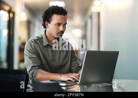 Un'altra e-mail e poi im fatto. un bel giovane uomo d'affari seduto da solo in ufficio e utilizzando il suo computer portatile. Foto Stock