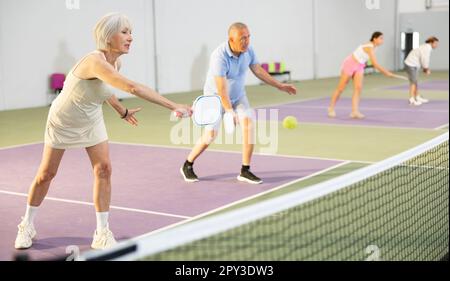 Donna anziana che gioca doppio pickleball match in squadra con l'uomo Foto Stock