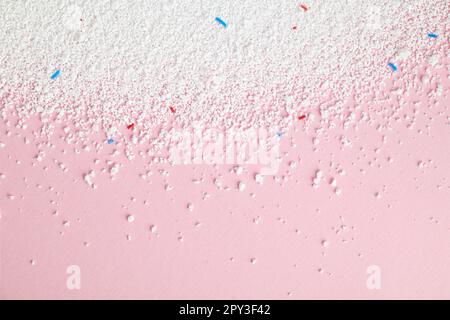Detersivo in polvere con granuli blu e rossi su fondo rosa primo piano, vista dall'alto. Foto Stock