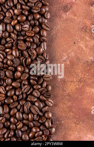 Chicchi di caffè arrostiti su sfondo marrone con texture dipinte a mano. Copiare lo spazio a destra dell'immagine. Foto Stock