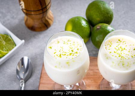 Deliziosa mousse di limone su una tovaglia marrone e sfondo bianco, con limoni interi e tagliati sullo sfondo, e un cucchiaio di metallo. PERSPECTIV Foto Stock