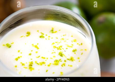 Deliziosa mousse di limone su una tovaglia marrone e sfondo bianco, con limoni interi e tagliati sullo sfondo, e un cucchiaio di metallo. Chiudere la vista Foto Stock