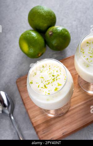 Deliziosa mousse di limone su un asse di legno e uno sfondo bianco da tavolo, con limoni interi e affettati sullo sfondo, e un cucchiaio di metallo. Foto Stock