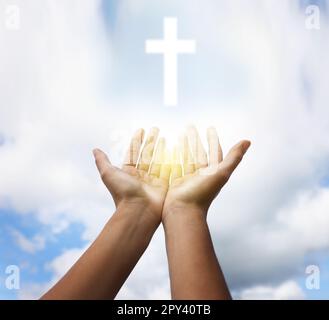 Donna che allunga le mani verso la silhouette a croce sul cielo blu, primo piano. Concetto di preghiera Foto Stock