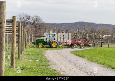 Lancaster County, Pennsylvania: 6 aprile 2023: Il trattore Green John Deere aratri campo preparandosi per la semina primaverile a frutteto locale. Foto Stock