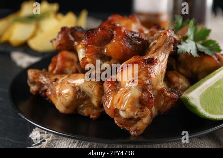 Deliziose ali di pollo fritte su piatto nero, primo piano Foto Stock