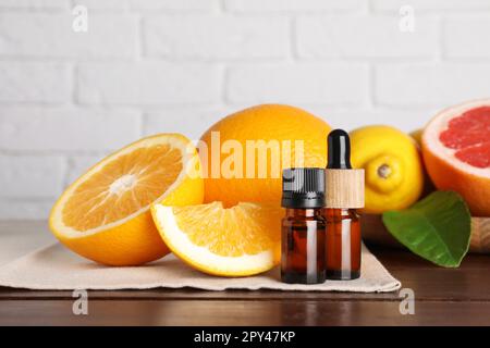 Bottiglie di oli essenziali con diversi agrumi e foglia su tavola di legno contro muro di mattoni bianchi Foto Stock