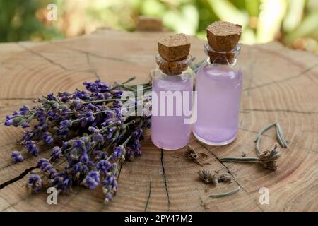 Bella lavanda fiori e bottiglie di olio essenziale su ceppo di legno, primo piano Foto Stock