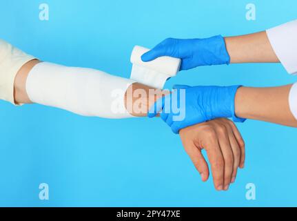 Medico che applica la bendatura medica sul braccio del paziente su sfondo azzurro, primo piano Foto Stock