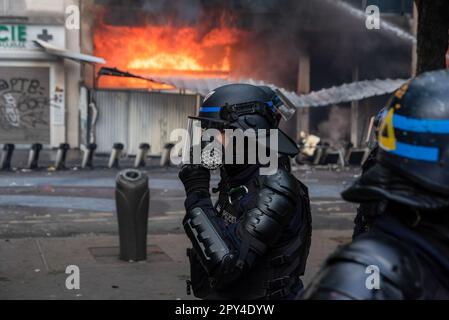 Un ufficiale di polizia è visto indossare una maschera a gas sul suo sfondo è un edificio in fiamme durante la dimostrazione Labor Day a Parigi. Centinaia di migliaia di persone hanno partecipato alla protesta del Labor Day a Parigi per chiedere di fermare la riforma molto impopolare delle pensioni. La protesta si è intensificata violenta in poco tempo. I manifestanti e la polizia si sono scontrati molte volte durante il giorno. I manifestanti si sono rotti nei negozi e hanno illuminato qualche cosa di infiammabile. La polizia ha dispiegato cannoni ad acqua e gas lacrimogeni per fermare la rivolta. (Foto di Krisztian Elek/SOPA Images/Sipa USA) Foto Stock