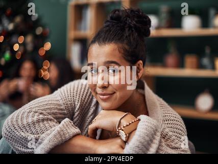 Natale è il momento di arricciarsi sul divano. Una bella giovane donna che si rilassa sul divano con i suoi amici sullo sfondo durante il Natale a. Foto Stock