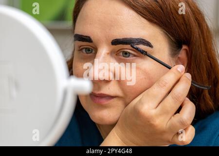 Ritratto di donna che fa sopracciglia se stessa guardando in specchio bianco all'interno della casa e avendo allergico dopo di esso Foto Stock