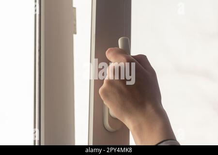 La mano dell'adolescente apre la finestra per far uscire l'aria camera Foto Stock