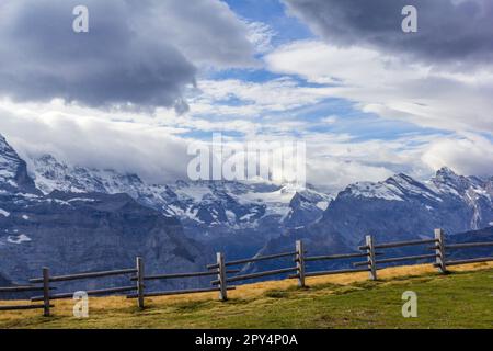 Il massiccio delle Alpi Jungfrau sotto le drammatiche nuvole con recinzione in legno in primo piano Foto Stock