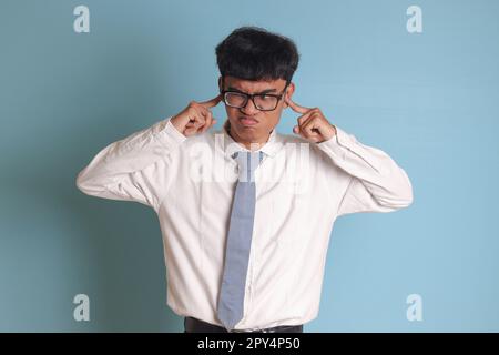 Studente indonesiano di scuola superiore che indossa una maglia bianca uniforme con cravatta grigia che copre le orecchie con le dita, cercando di evitare suoni o voci. Foto Stock