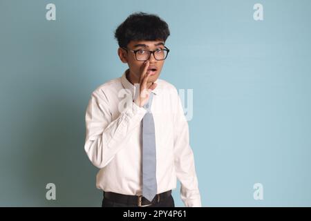 Studente indonesiano di scuola superiore che indossa una maglietta bianca uniforme con cravatta grigia che sussurra maligna conversazione, mano sulla bocca che dice segreto r Foto Stock