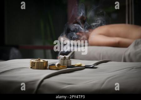 Trattamento di moxibustion - attrezzi cinesi tradizionali della medicina per la terapia di riscaldamento dei punti di agopuntura. Medicina cinese di erbe. Bruciatore in rame Moxibustion Foto Stock