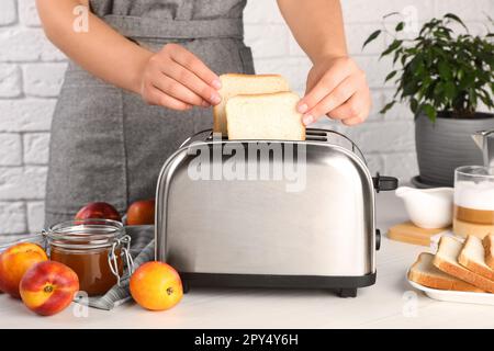 Donna che mette il pane nel tostapane in cucina, primo piano Foto Stock