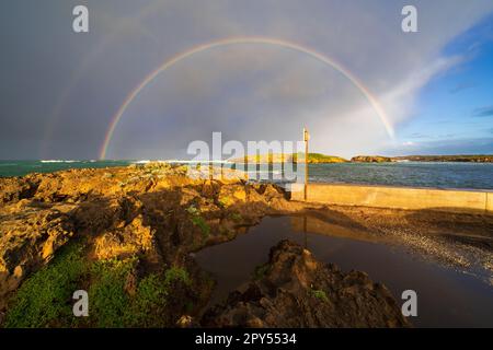 Un doppio arcobaleno di fronte a una nuvola buia di tempesta su una costa rocciosa a Warrnambool sulla Great Ocean Road a Victoria, Australia Foto Stock