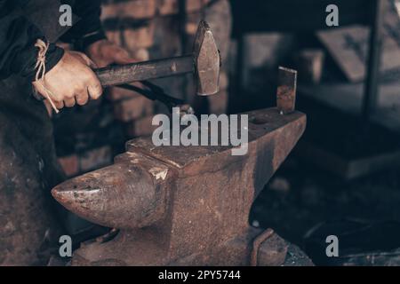 Lavorazione del metallo fabbro con martello e tenaglie su incudine in fucina. Farrier Strike Iron in officina. Lavorazione dei metalli. Foto Stock