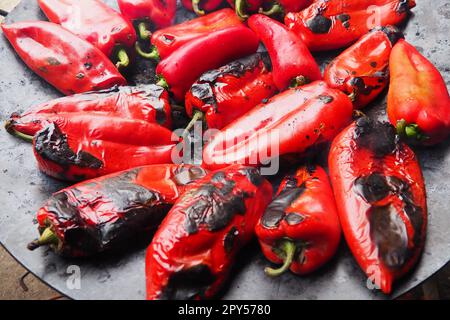 Arrostire deliziosi peperoni rossi per un sapore affumicato e una peeling veloce. Ricette per insalate balcaniche. Trattamento termico del raccolto di pepe su un cerchio metallico. I peperoni sono disposti su una placca da forno piatta per primo piano Foto Stock