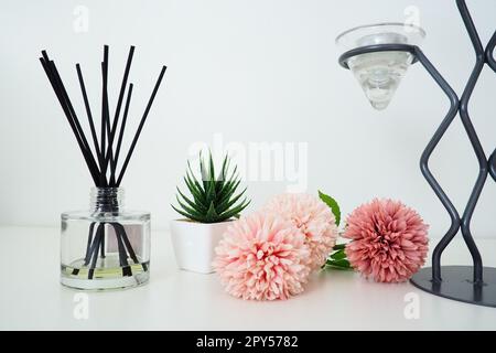 Composizione con bastoncini di incenso, olio essenziale in vaso di vetro e fiori artificiali di spugna rosa. Alto lampadario in metallo. Candela o vaso a righe grigie profumate. Aloe vegetale verde artificiale o kalanchoe Foto Stock