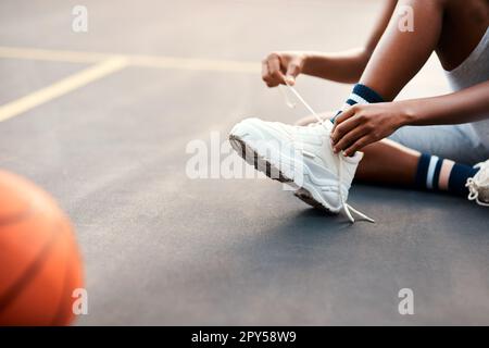 Assicurisi che i miei lacci sono legati. uno sportivo irriconoscibile seduto sul campo e legando i suoi lacci prima di giocare una partita di basket. Foto Stock