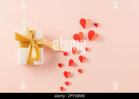 Vista dall'alto piatto di cuori di carta e scatola regalo su sfondo rosa pastello Foto Stock