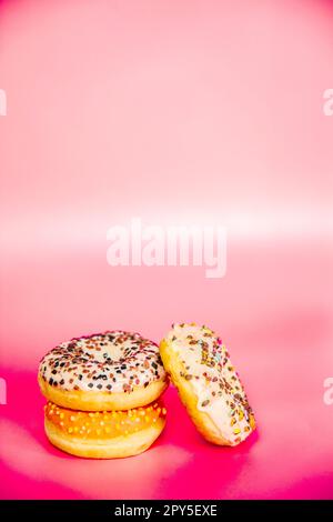 Ciambelle dolci impilate su uno sfondo rosa. Spazio copia, vari smalto e spruzzi di cioccolato chip, snack fast food dolci concetto Foto Stock