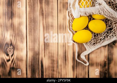 Composizione pasquale di cartolina di auguri, sfondo in legno per le festività e uova di colore giallo in sacchetto con corda Foto Stock