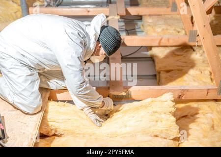 l'uomo isola il tetto e il soffitto della casa con lana di vetro Foto Stock